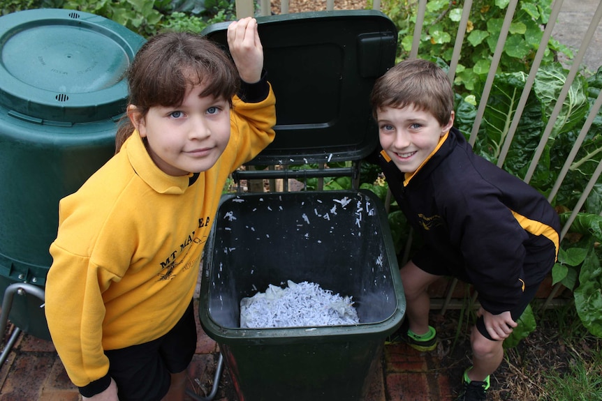 Two school students standing on either side of a bin full of shredded paper
