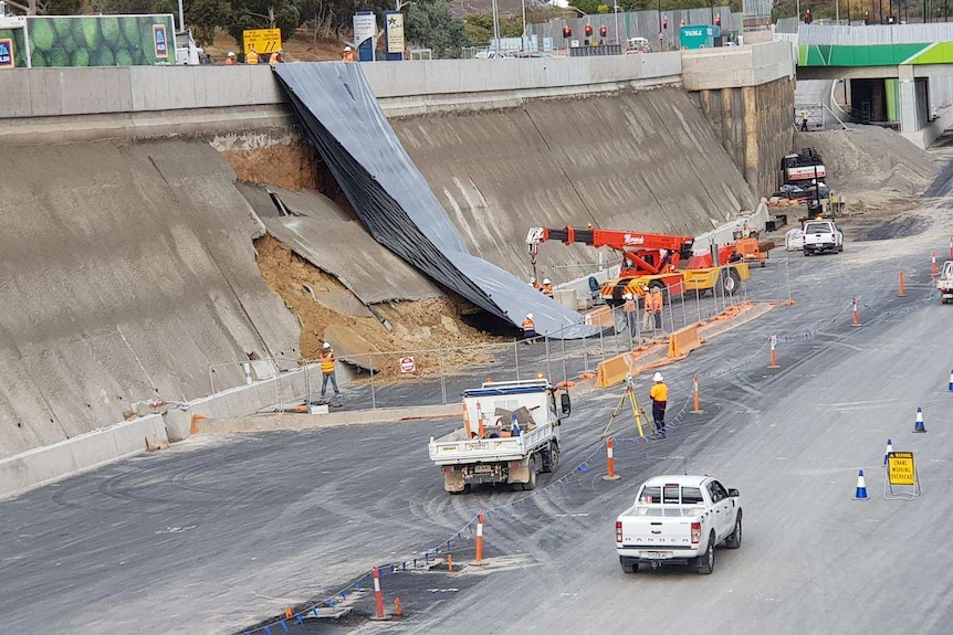 Workers put a tarp on a wall next to a freeway