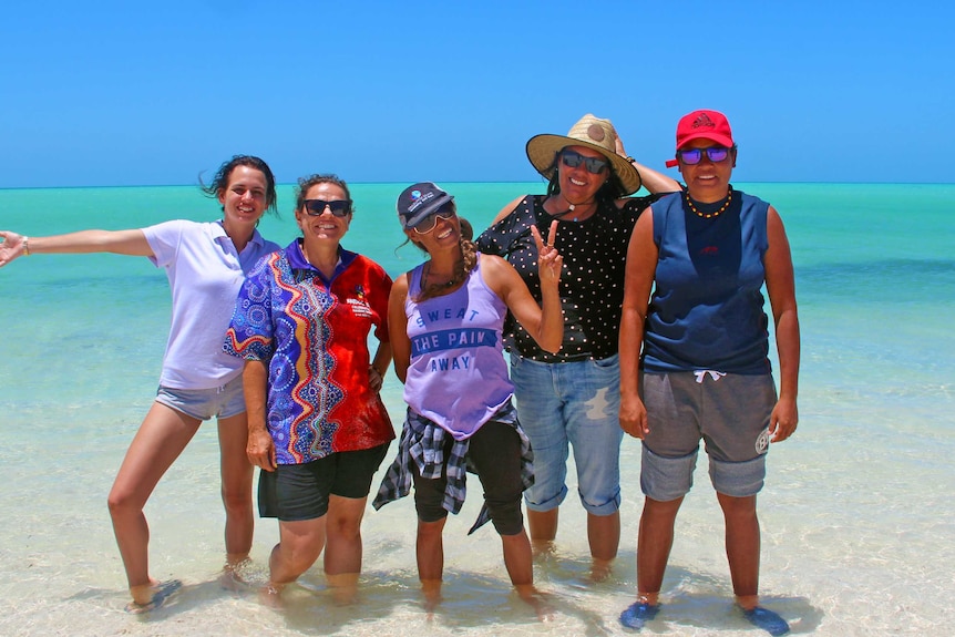 A group of Indigenous women standing in shallow water in the ocean.