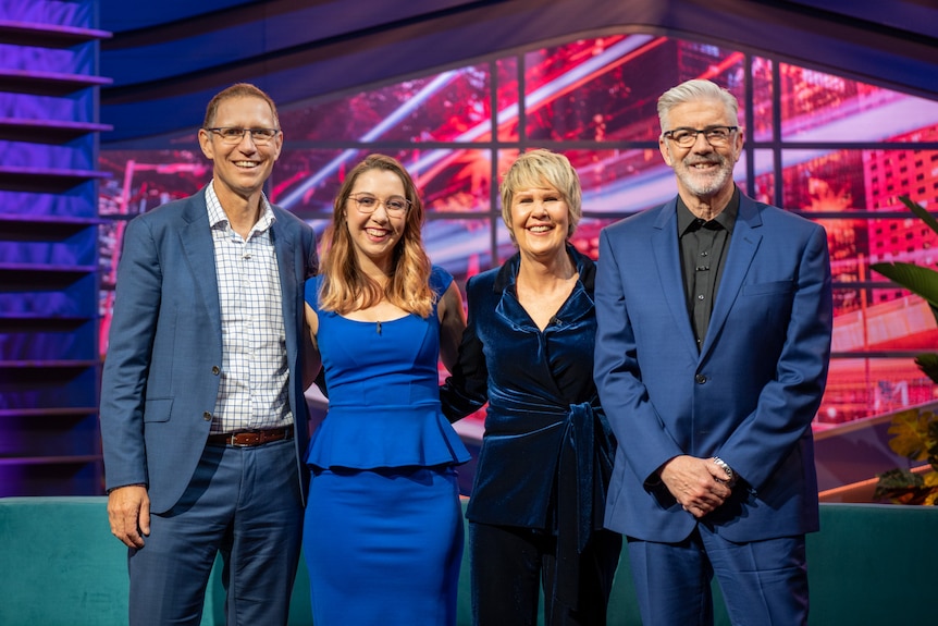 Kelly standing centre next to a woman with two men on either side in TV studio.