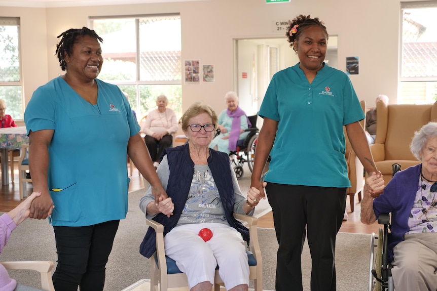 Women from Vanuatu in aged care uniforms holding hands with aged care residents.