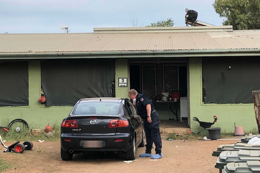 A policeman looks at a car parked outside a green house.