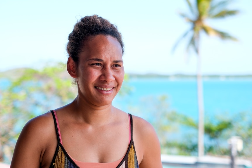 A woman smiles with the sea and a palm tree in the background