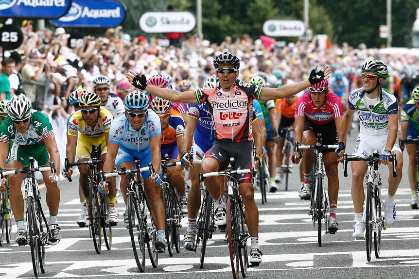 A cyclist throws his arms out to his sides in celebration after winning a Tour de France stage.