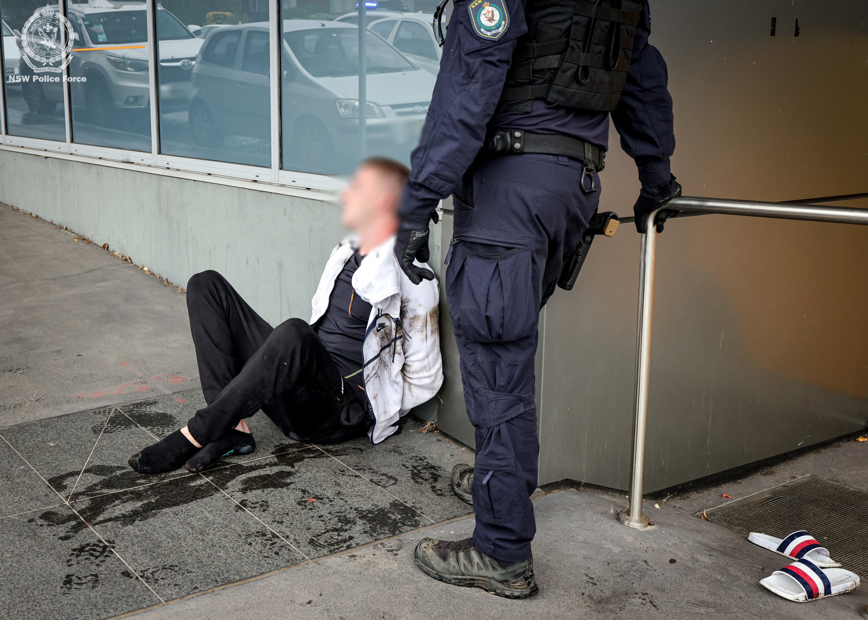 A man sits on the floor with a police officer stood next to him