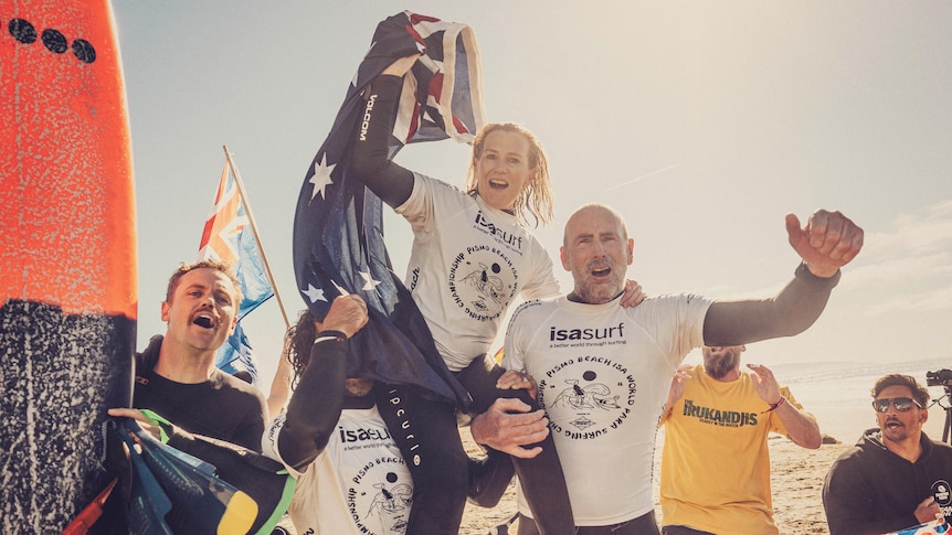 Para surfer Emma Dieters is on the shoulders of two men, she is celebrating and holding an Australian flag