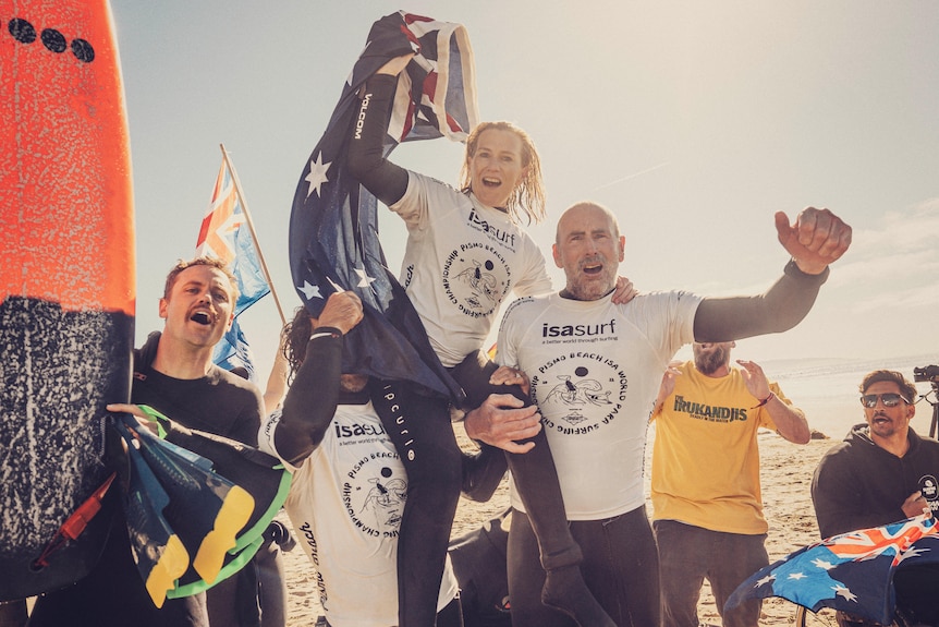 Para surfer Emma Dieters is on the shoulders of two men, she is celebrating and holding an Australian flag