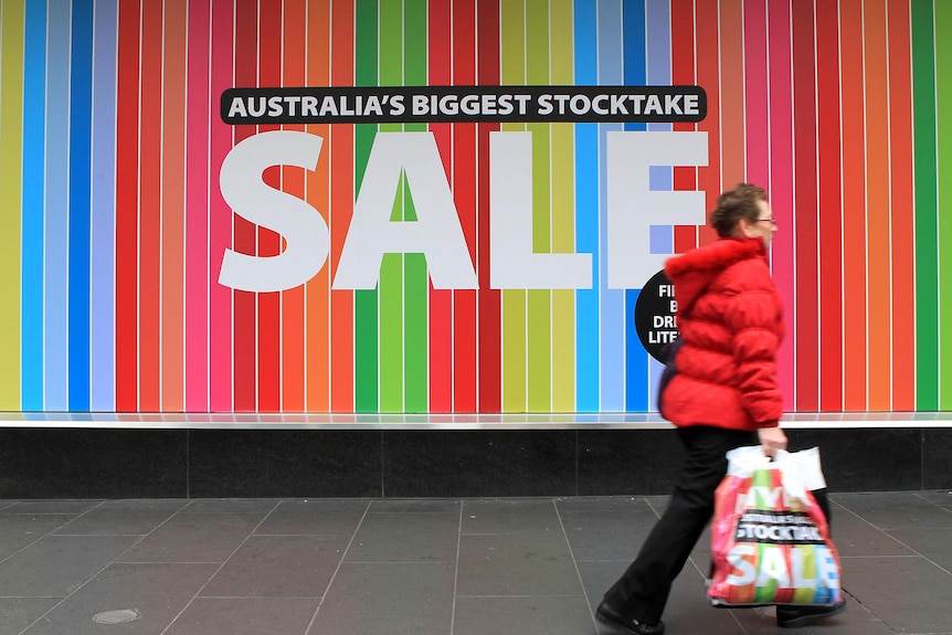 A woman walks past a store displaying a sale sign.