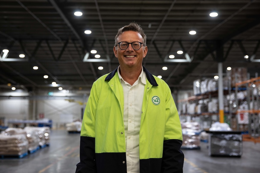 A man with glasses stands in a large warehouse.