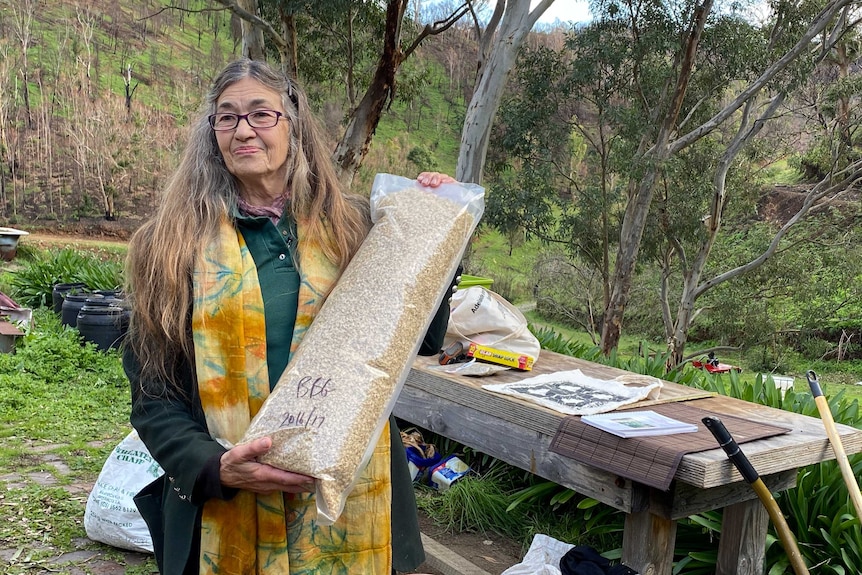 A woman holds up a large bag of native grass seeds