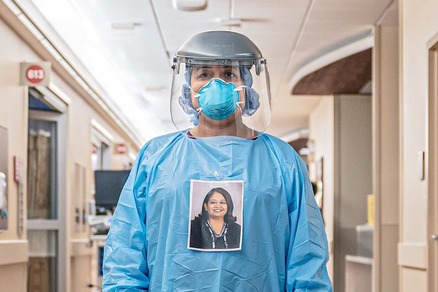 A woman in full PPE with a photo of her face taped to her chest