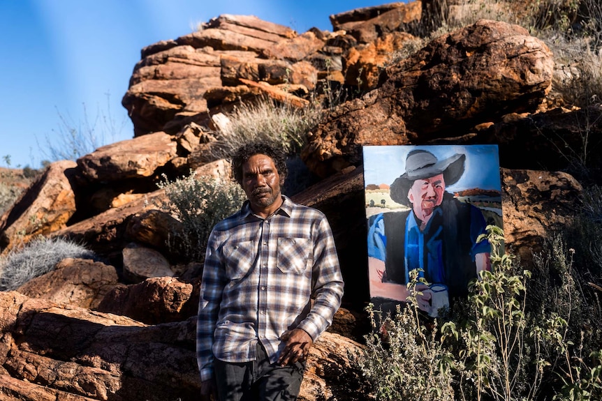 Vincent Namatjira stands with his portrait of Slim Dusty on Country 