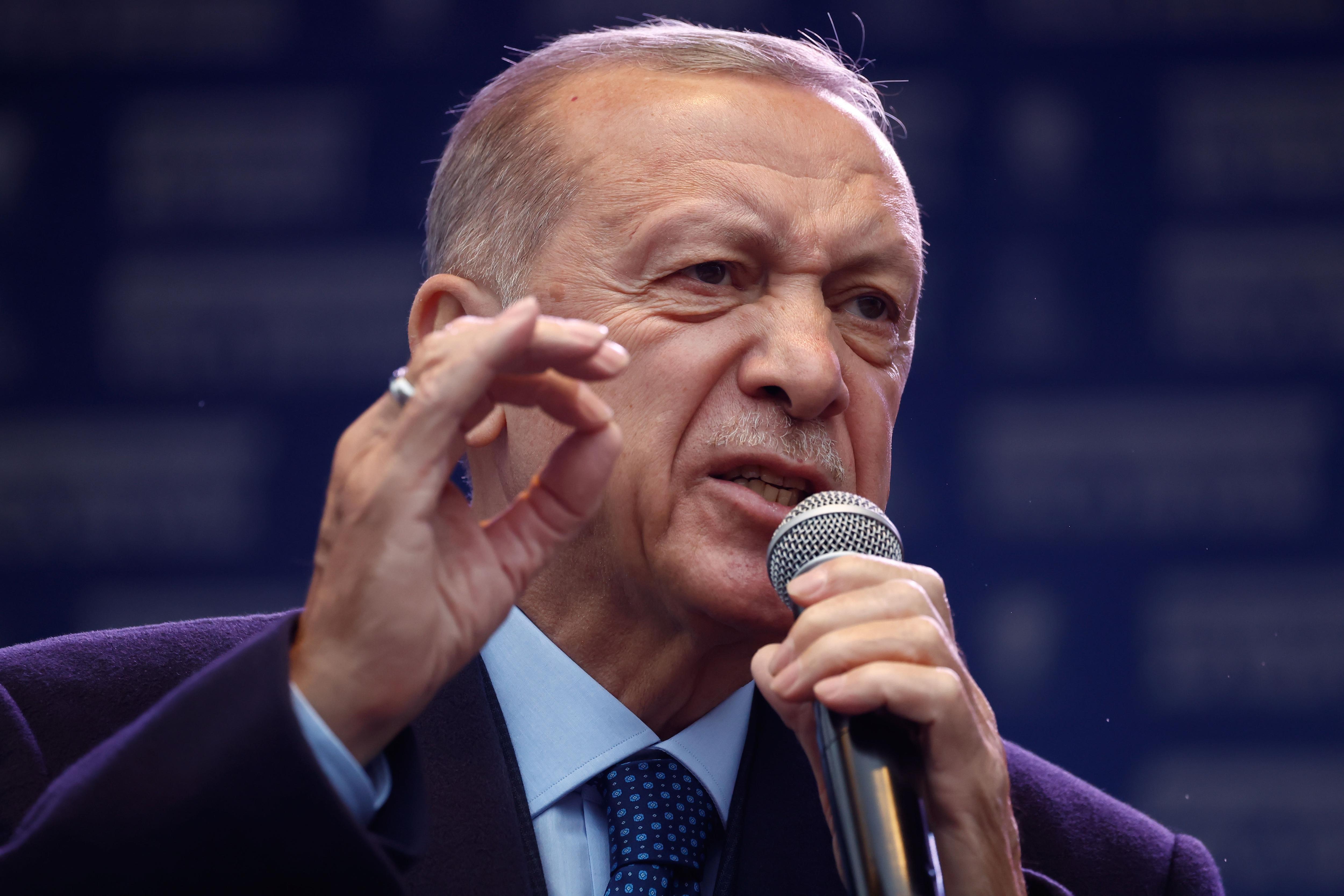 An older Turkish man in a suit yells into a microphone.
