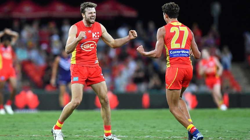 Two AFL teammates run to each other in celebration after winning a game,