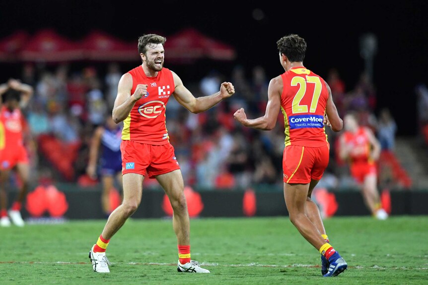 Two AFL teammates run to each other in celebration after winning a game,