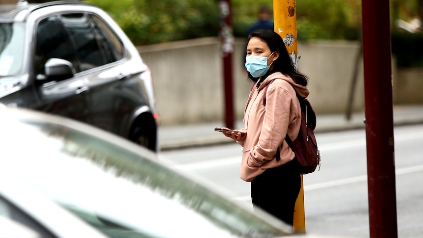 A picture of a woman wearing a hoodie and a mask, carrying a backpack.