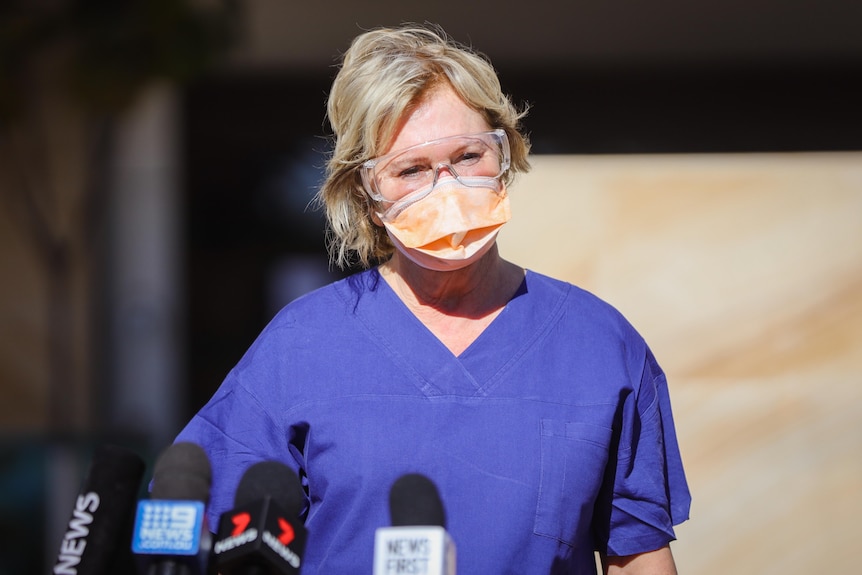 a woman wearing goggles and a face mask, surrounded by microphones