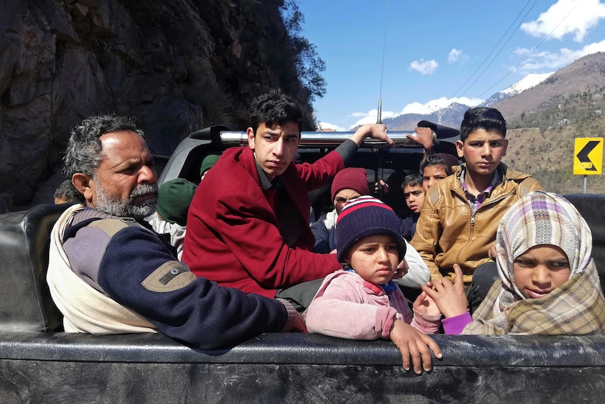 A family sits in the back of a truck driving down a country road.