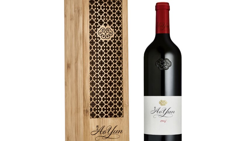 a bottle of red wine standing next to its wooden display case