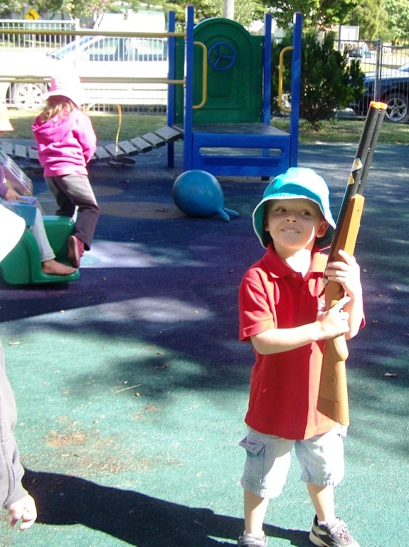 Preschool aged boy stands holding a cardboard/paper gun.