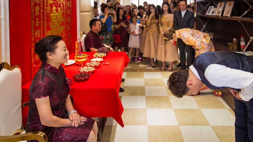 The groom and the bride bowed to their parents in front of a traditional Chinese style setting.