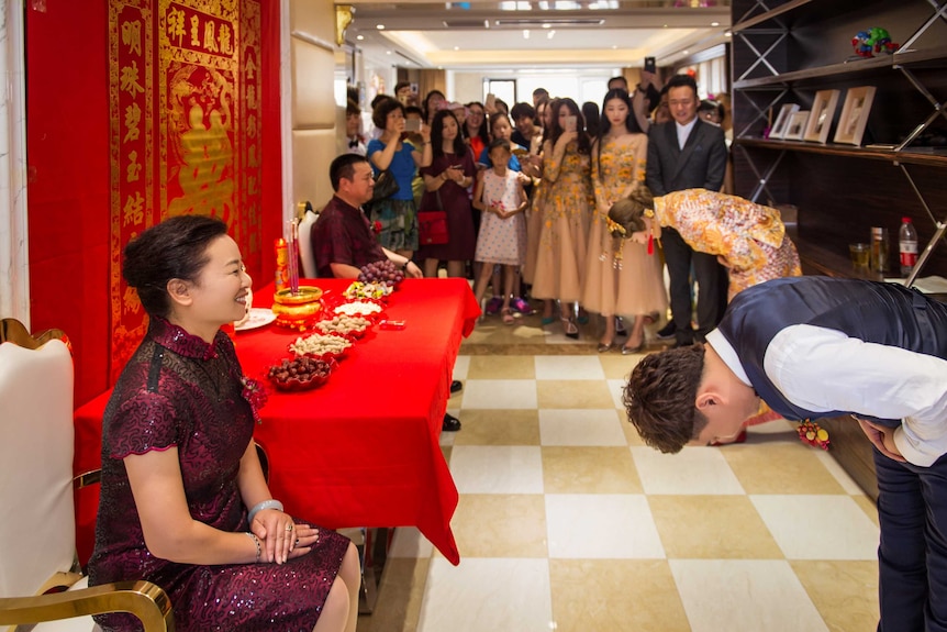 The groom and the bride bowed to their parents in front of a traditional Chinese style setting.