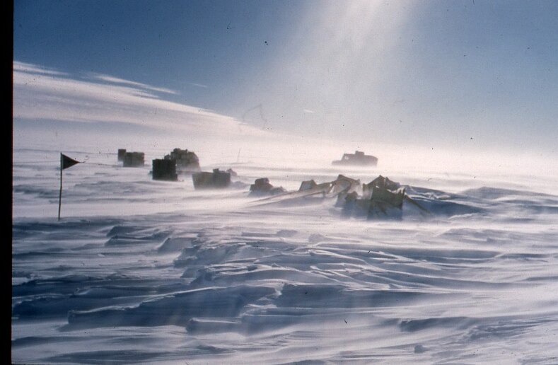 Vehicles and a flag are seen in the distance amid snow.