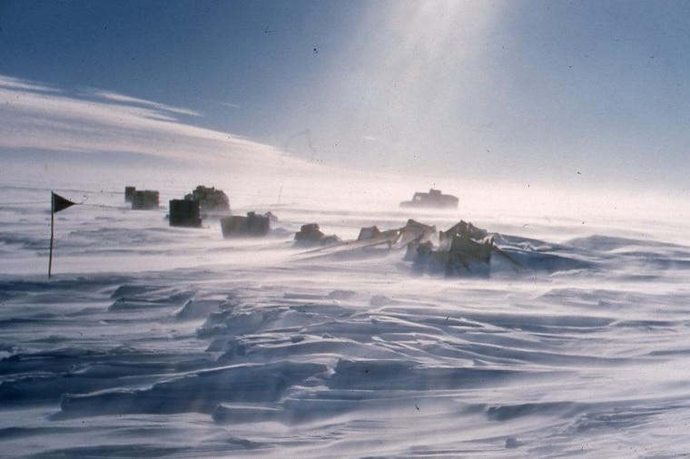 Vehicles and a flag are seen in the distance amid snow.