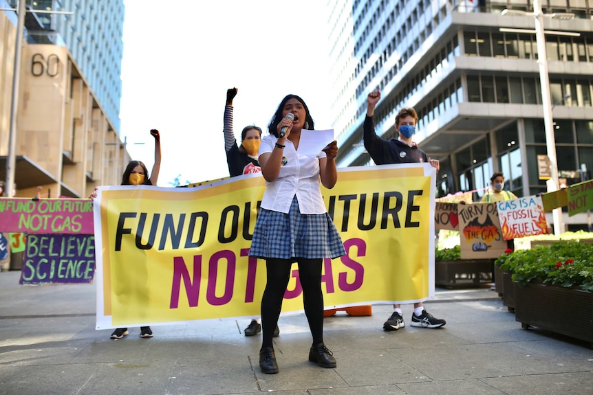 Natasha speaks into a microphone as she marches in front of a large sign.