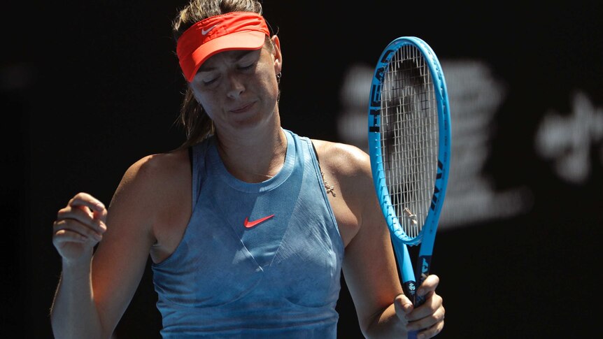 A female tennis player closes her eyes and shrugs her shoulders with her racquet in her left hand