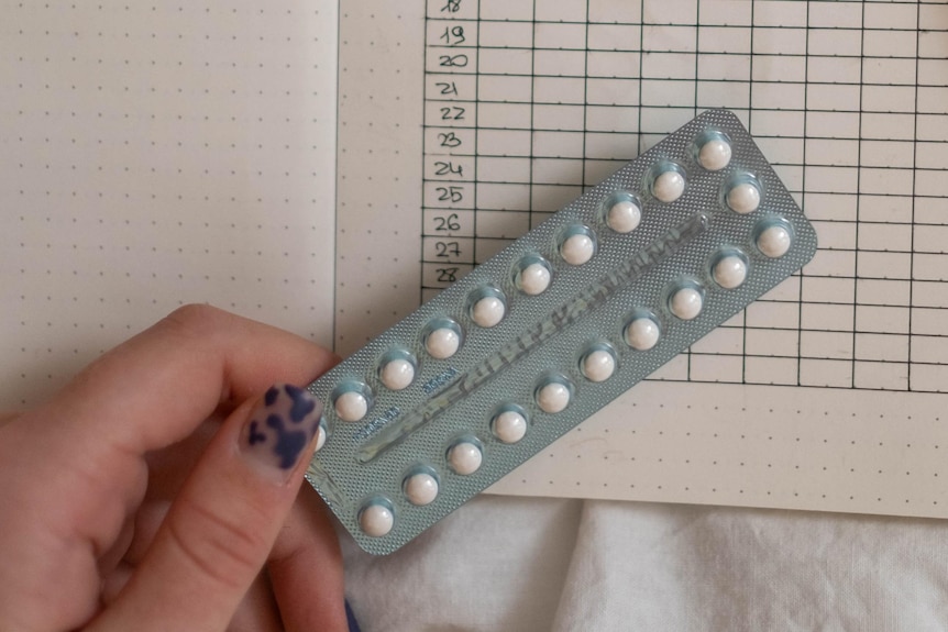 Person's hand with blue nailpolish design holding onto the pill