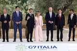 Six men and a woman, all wearing suits, stand on a podium with the words G7 Italia 2024 on it.