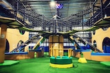 An indoor playground with greens floor and slides and high bridges.