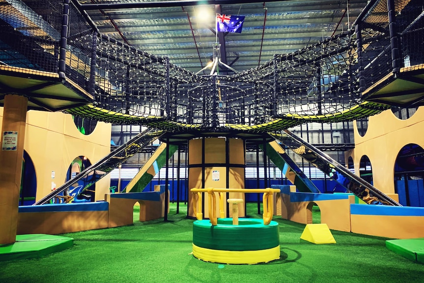 An indoor playground with greens floor and slides and high bridges.
