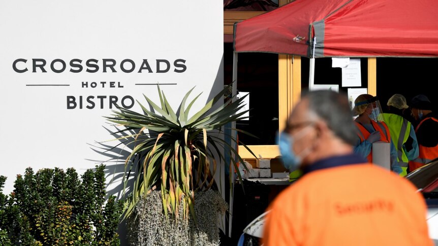 A man in a high-vis vest and mask stands outside the Crossroads Hotel during coronavirus testing.