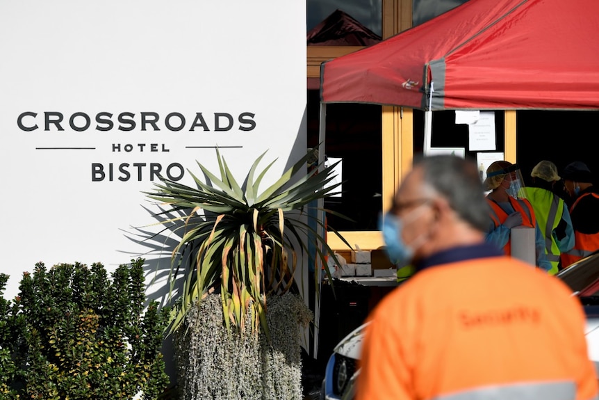 A man in a high-vis vest and mask stands outside the Crossroads Hotel during coronavirus testing.