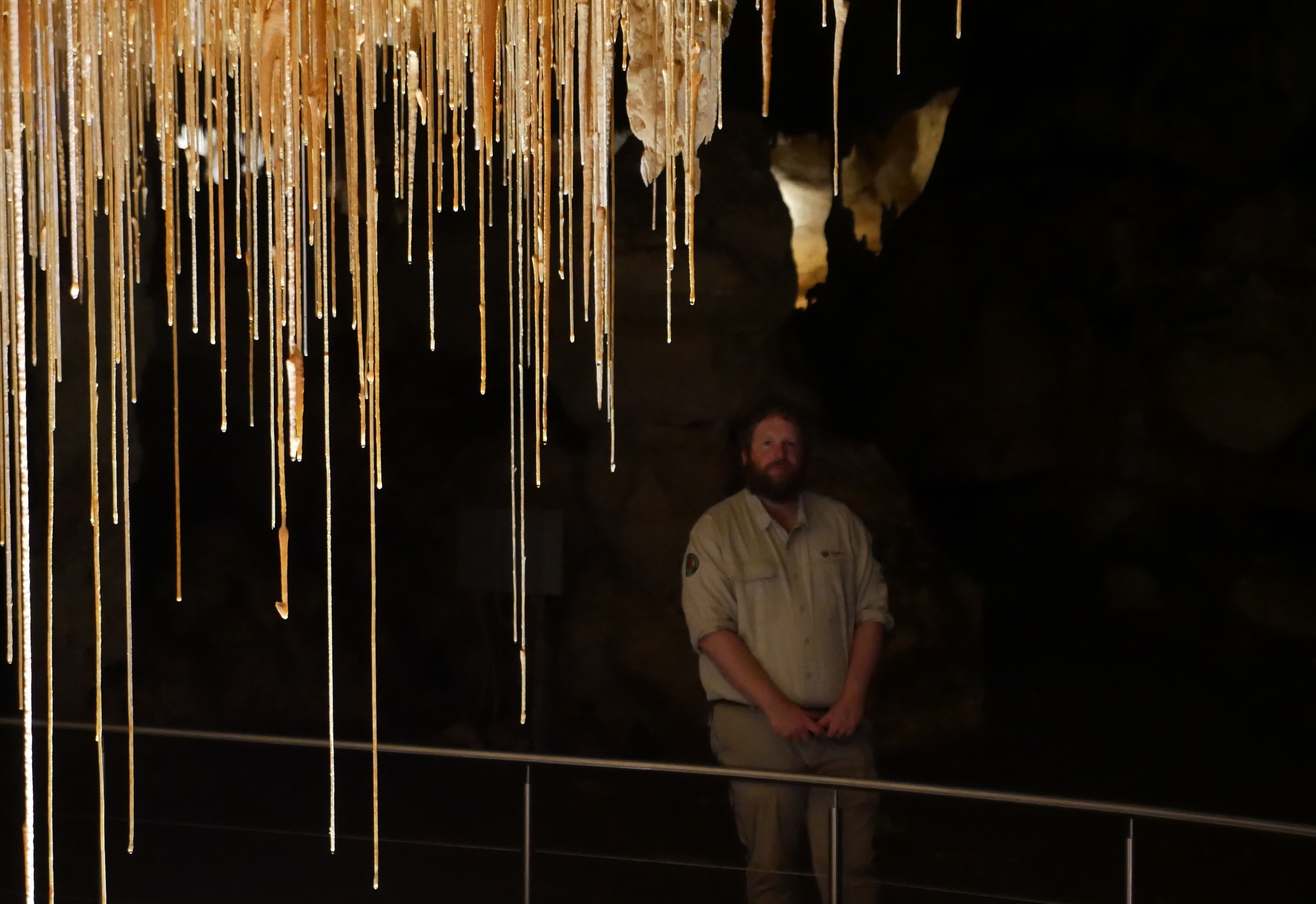 A man standing behind stalactites in a cave. 