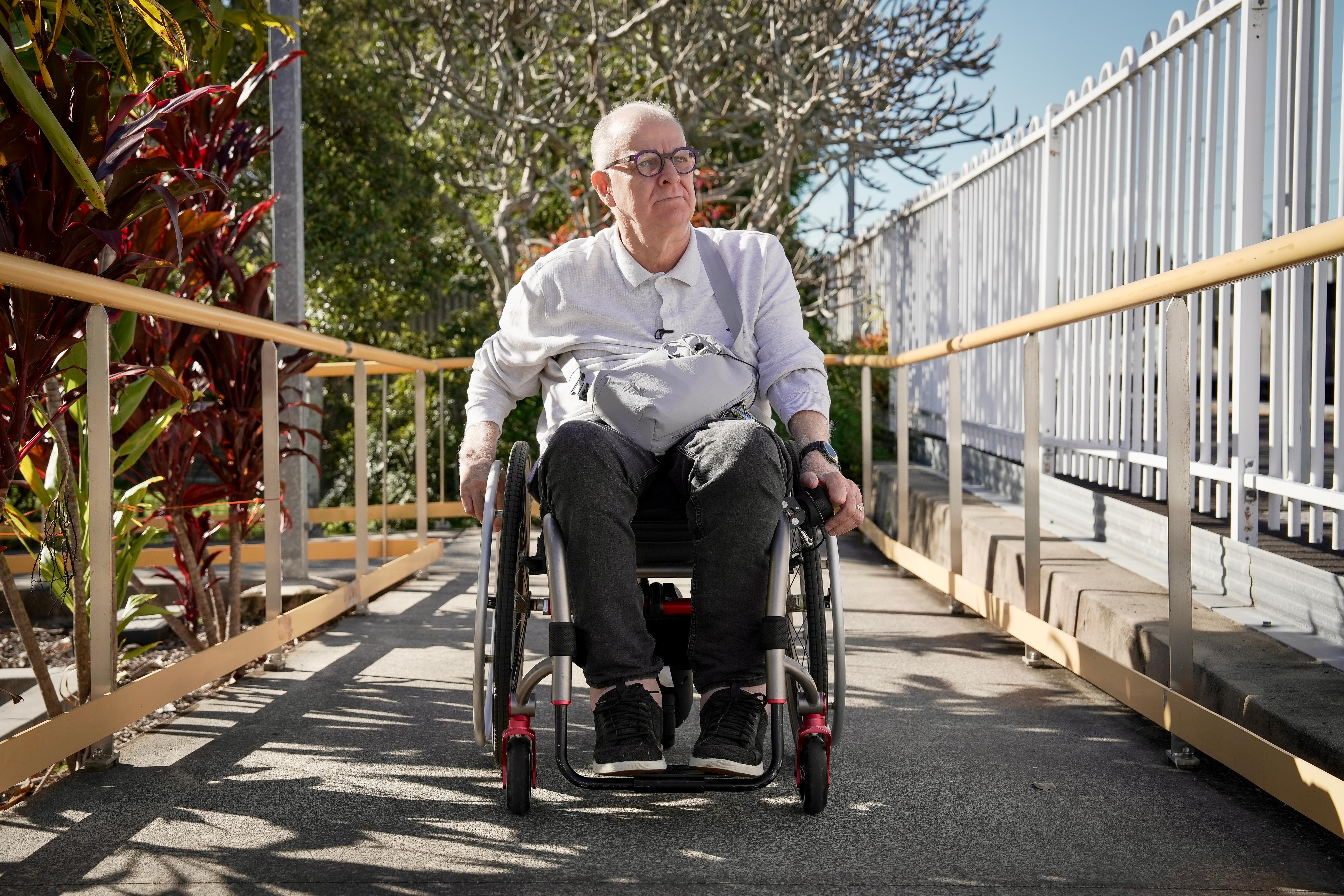 A middle aged white man with short grey hair. He's in a wheelchair rolling up a ramp