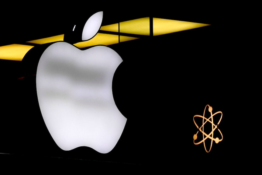 The Apple tech company logo of an apple is illuminated in white against a black background