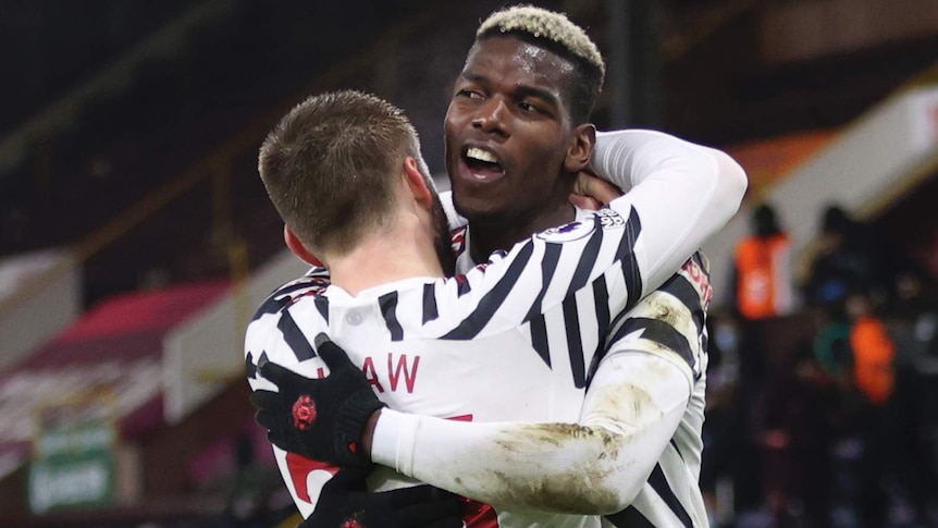 Paul Pogba hugs Luke Shaw, with both players wearing a white shirt with black stripes