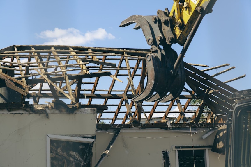 A bulldozer smashes through a roof frame on a house coming down