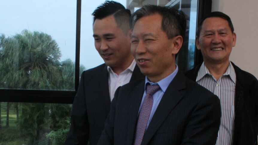 Three Chinese men standing in front of a window with trees in background