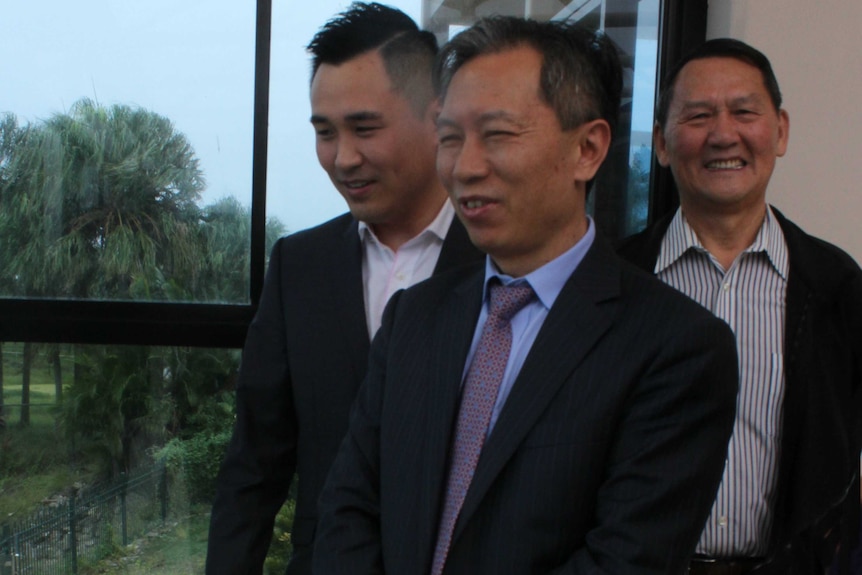 Three Chinese men standing in front of a window with trees in background