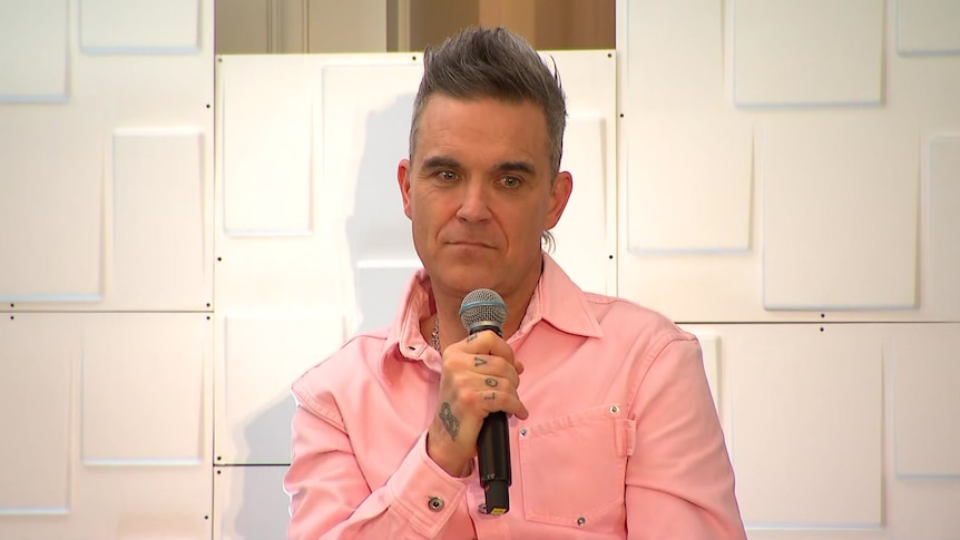 Robbie Williams sit with a microphone in hand