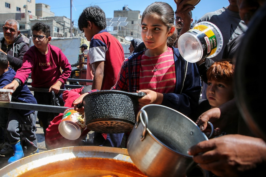 Children with pots stand around a huge pot of soup 