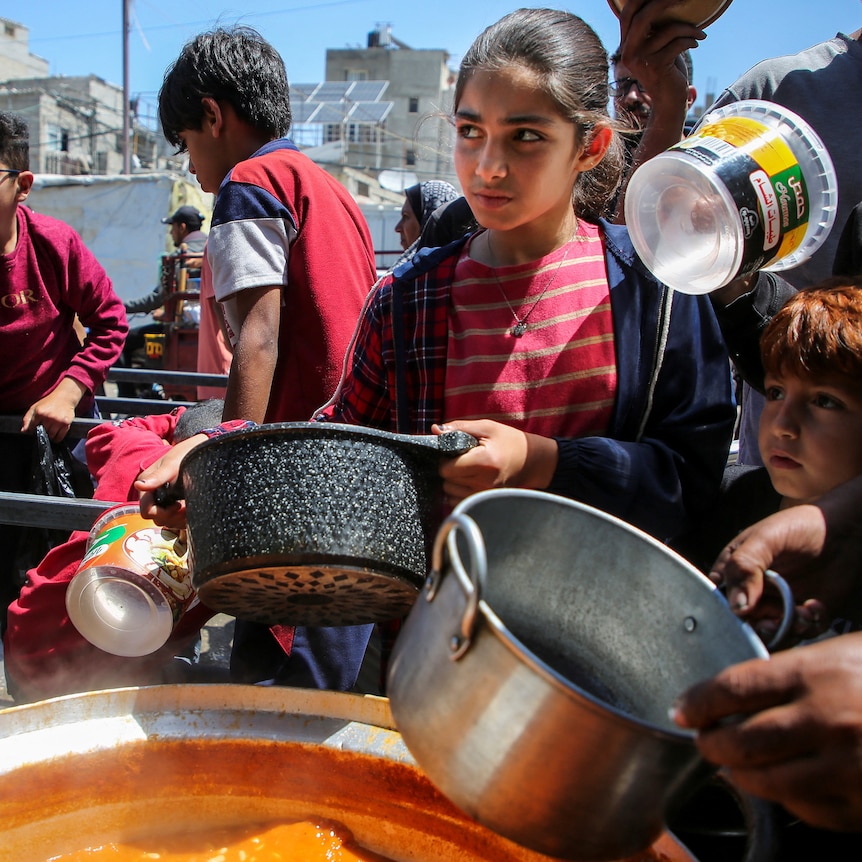 Children with pots stand around a huge pot of soup 