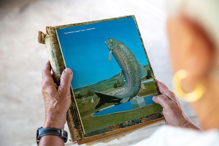 A photo of a woman holding an image of an old rainbow trout statue