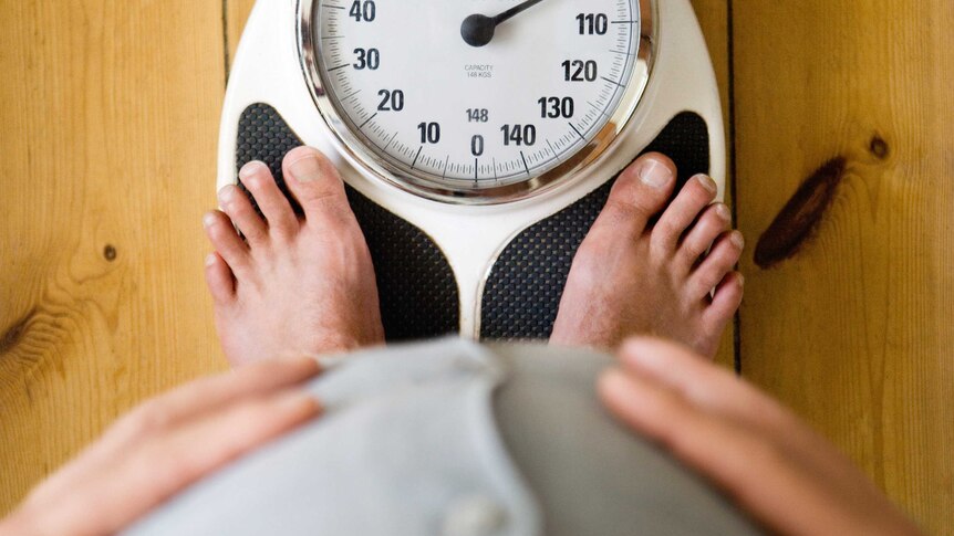 An overweight man stands on a scale that reads 100 kilograms