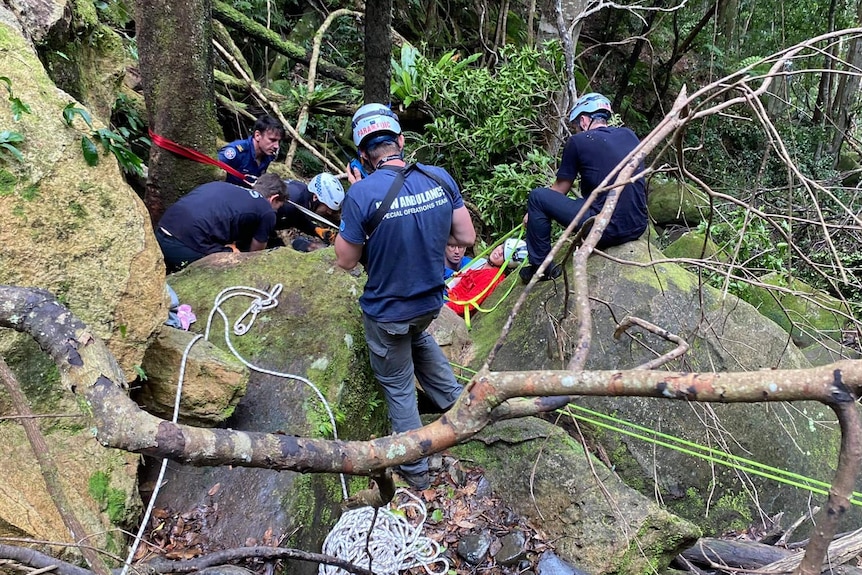 emergency workers attend to a man in the bush whose leg was trapped under a boulder