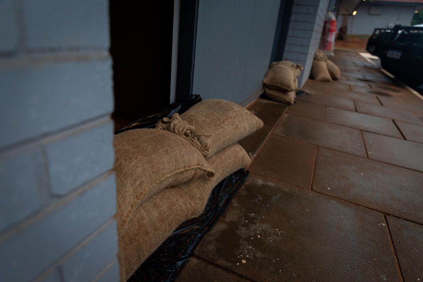 Sandbags propped up in front of doorways, view from a sidewalk. Photo. Four in the foreground and multiple in the background.